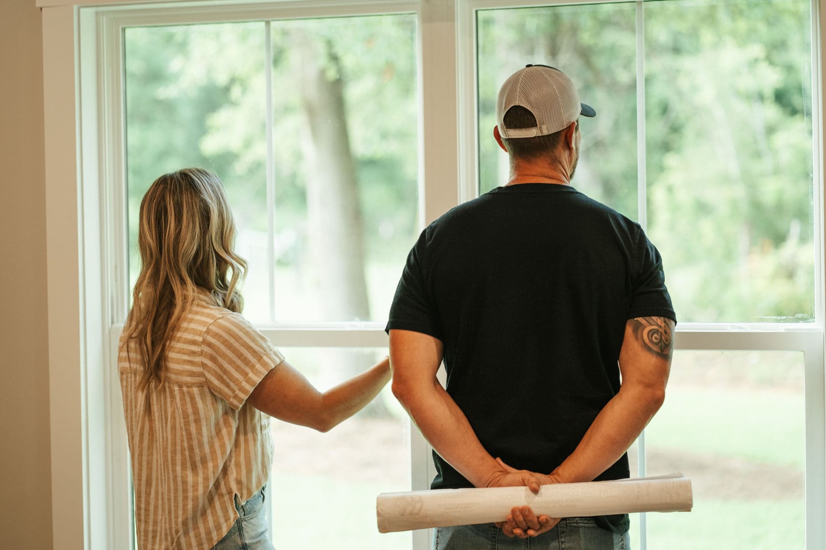 the owners of live oak custom homes looking out of a window holding plans for a new foundation